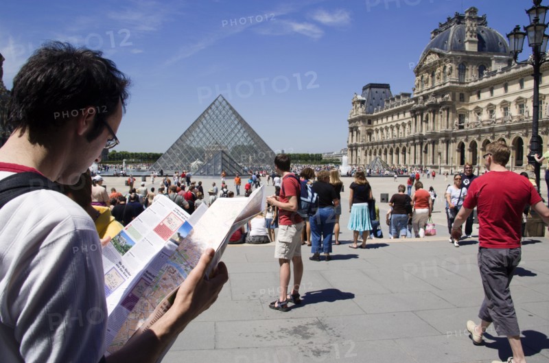 FRANCE, Ile de France, Paris, Tourists reading a guide in the square outside the pyramid entrance to the Musee du Louvre