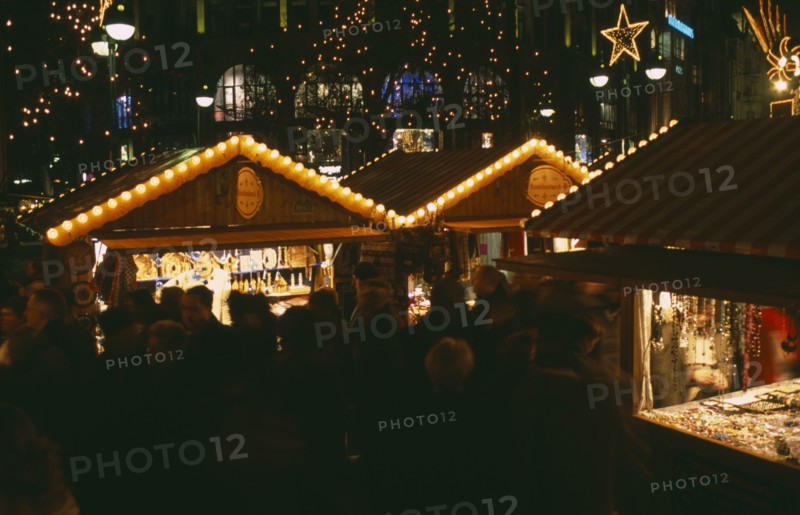 GERMANY, Berlin, Breitscheidplatz. Christmas Market. People gathered around Illuminated stalls at night. Lights and star decorations behind
