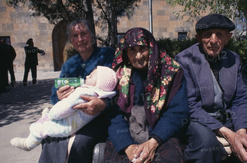 ARMENIA, Echmiadzin, Woman bottle feeding baby beside elderly couple sitting in sunshine.
