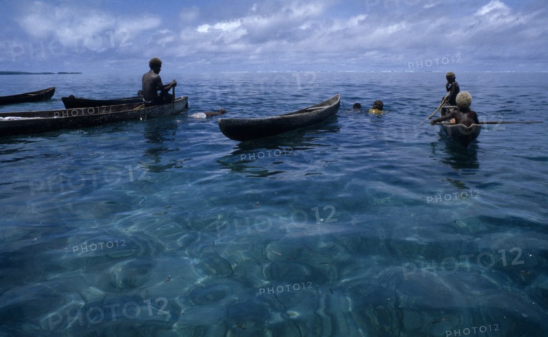 PACIFIC ISLANDS, Melanesia, Solomon Islands, "Malaita Province, Lau Lagoon. Spear fishing from wooden dug out canoes.  Dark turquoise sea with light reflections and blue sky."