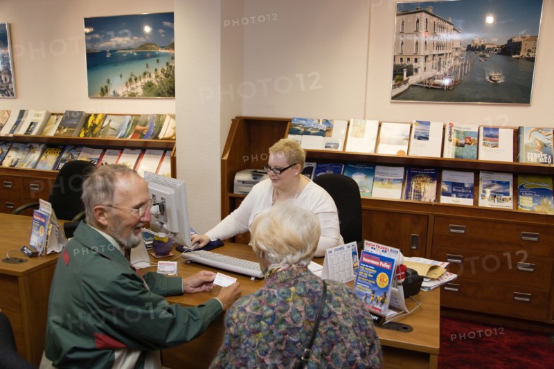 ENGLAND, West Sussex, Chichester, Male and female customer in a Travel Agents office discussing their holiday arrangements with a female travel consultant