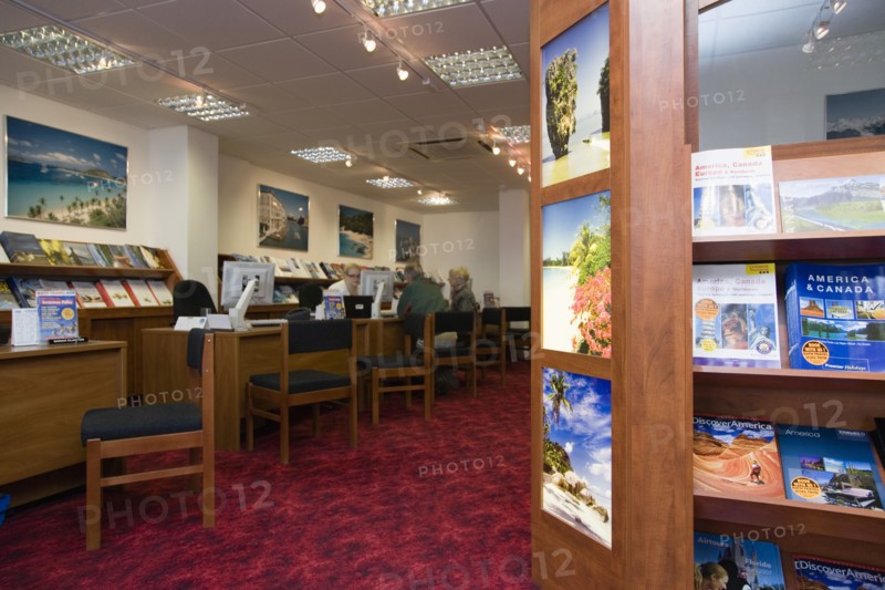 ENGLAND, West Sussex, Chichester, Male and female customer in a Travel Agents office discussing their holiday arrangements with a female travel consultant with travel brochures on shelves in the foreground