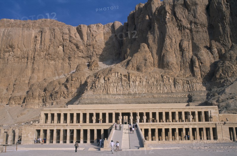 EGYPT, Nile Valley, Thebes, Deir el-Bahri. Hatshepsut Mortuary Temple. Visitors walking towards ramped entrance with limestone cliffs behind.