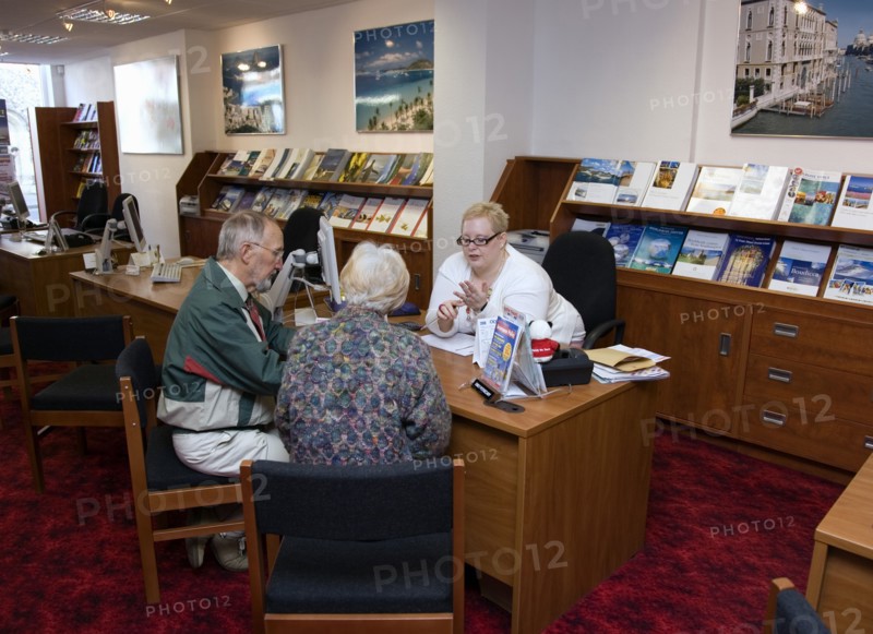 ENGLAND, West Sussex, Chichester, Male and female customer in a Travel Agents office discussing their holiday arrangements with a female travel consultant