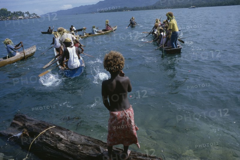PACIFIC ISLANDS, Melanesia, Solomon Islands, "Malaita Province, Lau Lagoon.  Child watching wedding party depart by canoe.  Note rafia head dresses of rowers."