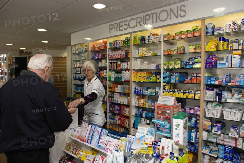 ENGLAND, East Sussex, Shoreham by sea, Interior of high street dispensing chemist  with male customer collecting his prescription from the pharmacist assistant behind the counter