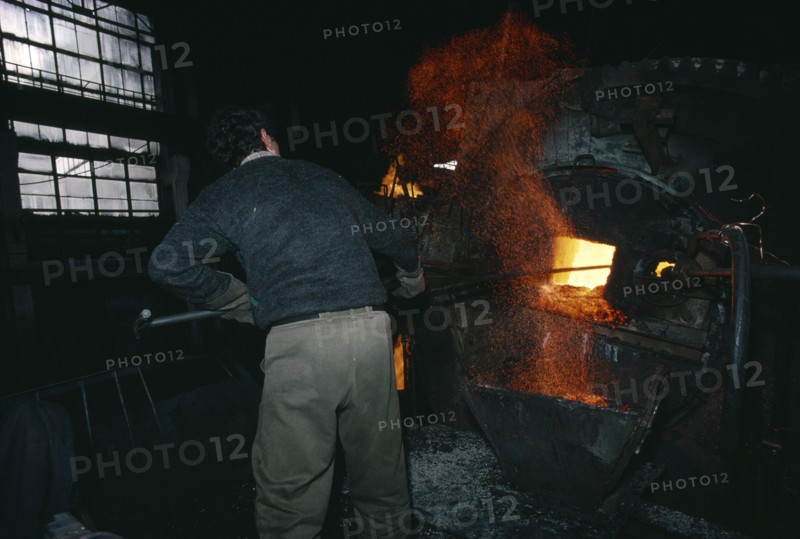 ARMENIA, Yerevan, Cable factory worker in front of furnace with flying sparks.