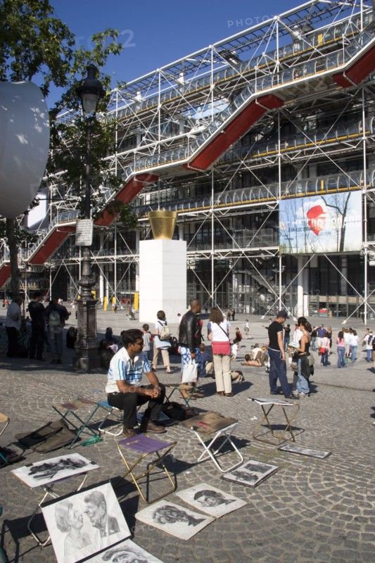 FRANCE, Ile de France, Paris, Tourists watching a street performer in the square outside the Pompidou Centre in Beauborg Les Halles with artists selling their work on the pavement in the foreground