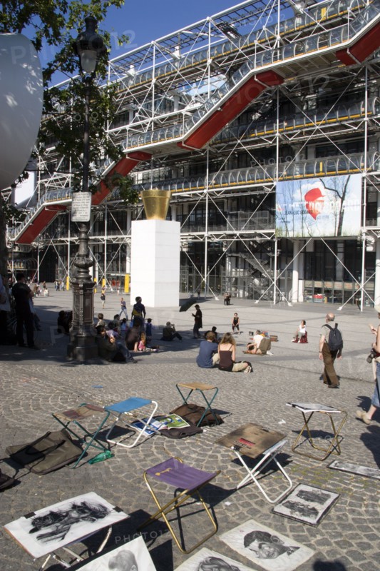 FRANCE, Ile de France, Paris, Tourists watching a street performer in the square outside the Pompidou Centre in Beauborg Les Halles with artists selling their work on the pavement in the foreground