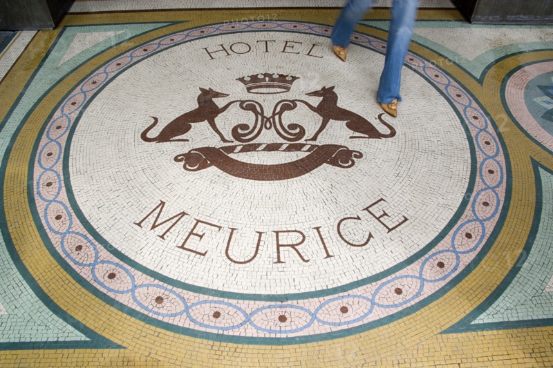 FRANCE, Ile de France, Paris, Woman walking across a mosaic with a crest and the words Hotel Meurice on the pavement outside the entrance door to the five star hotel in the Rue de Rivoli