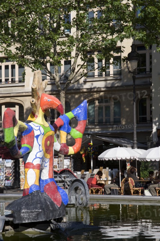 FRANCE, Ile de France, Paris, People sitting at tables under umbrellas beside the colourful contemporary fountains by Niki de Saint Phalle and Jean Tinguely in Place Igor Stravinsky beside the Pompidou Centre in Beauborg Les Halles