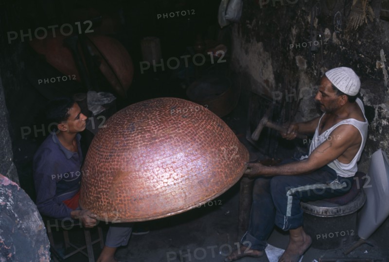 EGYPT, Cairo Area, Cairo, Coppersmith working on a large bowl in the Khan el-Khalil area of  famous narrow streets of bazaars.