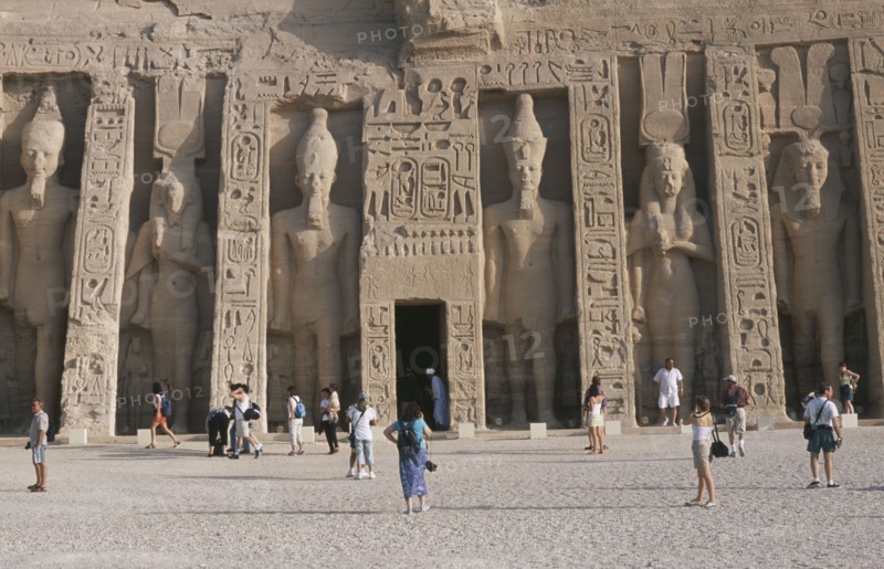 EGYPT, Nile Valley, Abu Simbel, Hathor Temple . Built for Ramses II's wife Nefertari. Six standing statues caved into facade. Visitors walking in the grounds.