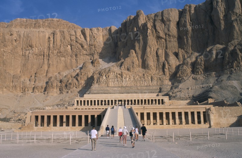 EGYPT, Nile Valley, Thebes, Deir el-Bahri. Hatshepsut Mortuary Temple. Visitors walking towards ramped entrance with limestone cliffs behind