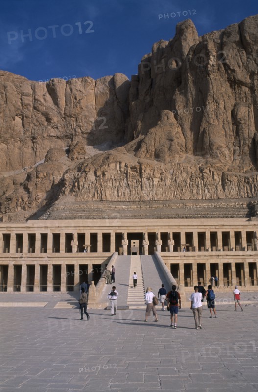 EGYPT, Nile Valley, Thebes, Deir el-Bahri. Hatshepsut Mortuary Temple. Visitors walking towards ramped entrance with limestone cliffs behind.