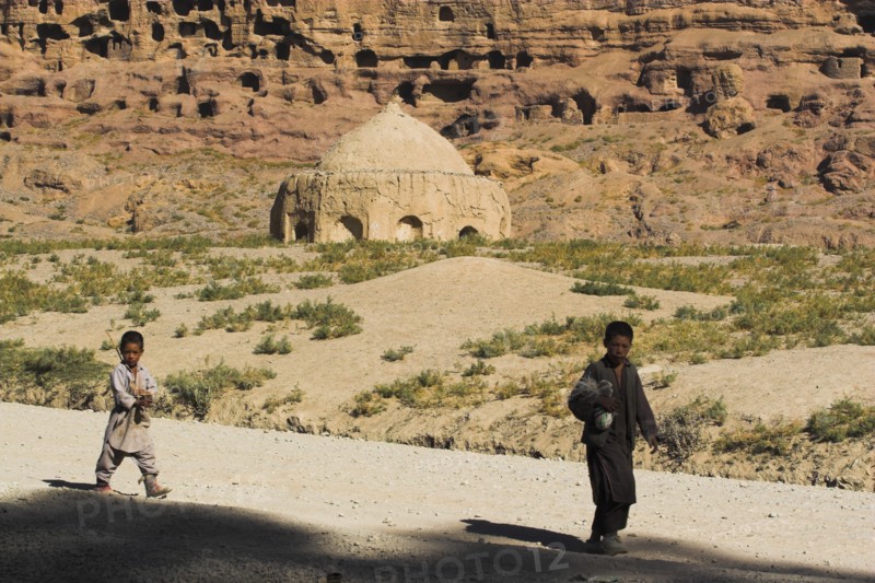 AFGHANISTAN, Bamiyan Province, Bamiyan, Boys walk past tomb near empty niche where the famous carved Budda once stood (destroyed by the Taliban in 2001)