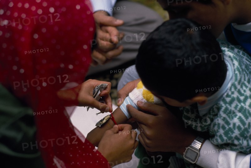 ENGLAND, Religion, Woman tying thread on arm of boy during the Sacred Thread ceremony. The Hindu male rite of passage ceremony