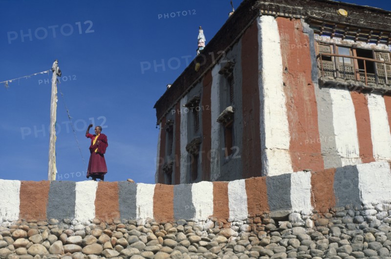 NEPAL, Mustang, Tsarang Gompa, "Tibetan Buddhist monk looking out from monastery terrace, shielding his eyes from the sun."