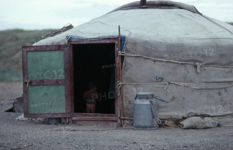 MONGOLIA, Architecture, Young child standing inside open doorway of yurt wearing just a jumper and no trousers.