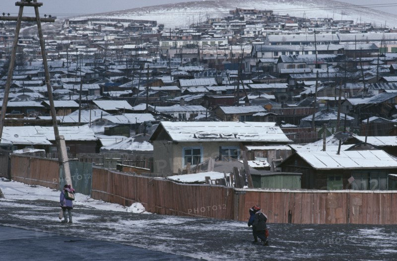 MONGOLIA, Ulan Bator, Snow covered rooftops of housing in city suburbs in winter with children wrapped up in warm clothing walking along road in foreground.