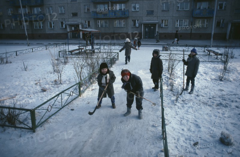 MONGOLIA, Ulan Bator, Children playing ice hockey along pavements in winter snow.