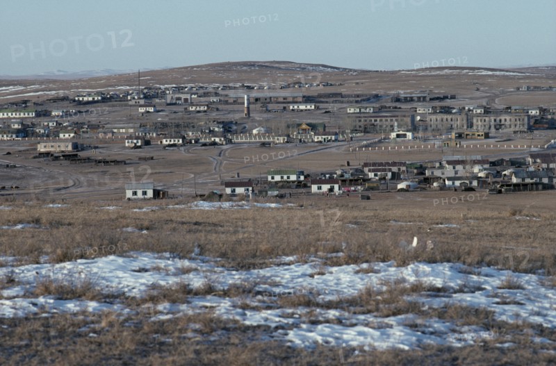 MONGOLIA, Gobi Desert, Tsagaan Ovoo, View towards typical small town in open landscape with patches of melting snow in the foreground.