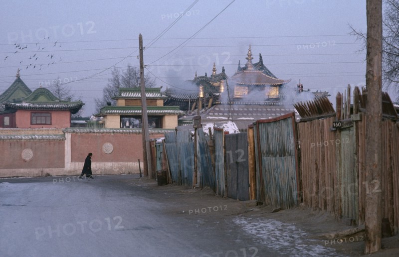 MONGOLIA, Ulan Bator, Gandan Monastery.  View along street towards monastery rooftops with passing figure wearing winter coat and hat.