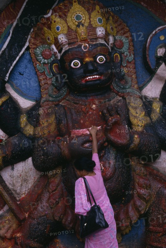 NEPAL, Kathmandu, Woman making offerings at the Kala Bhairab or black Shiva in Durbar Square representing the fearsome Tantric form of Shiva in Nepal.