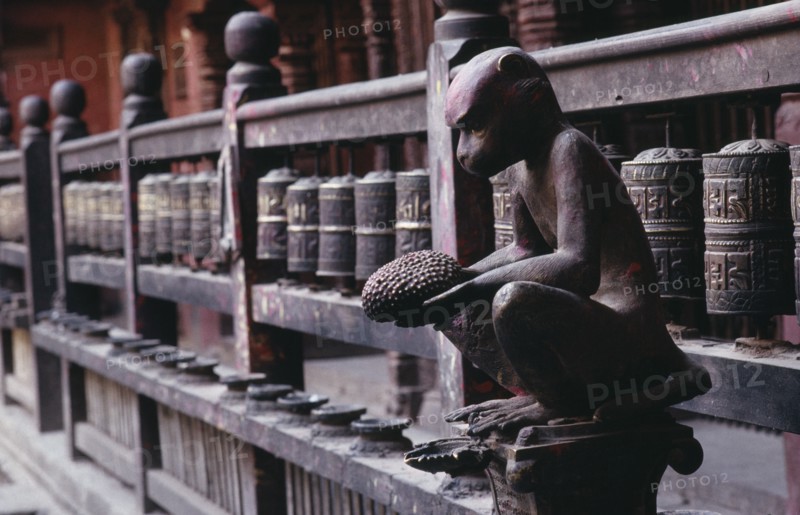 NEPAL, Patan, Carving of monkey holding a jack fruit in front of mane or prayer wheels behind.