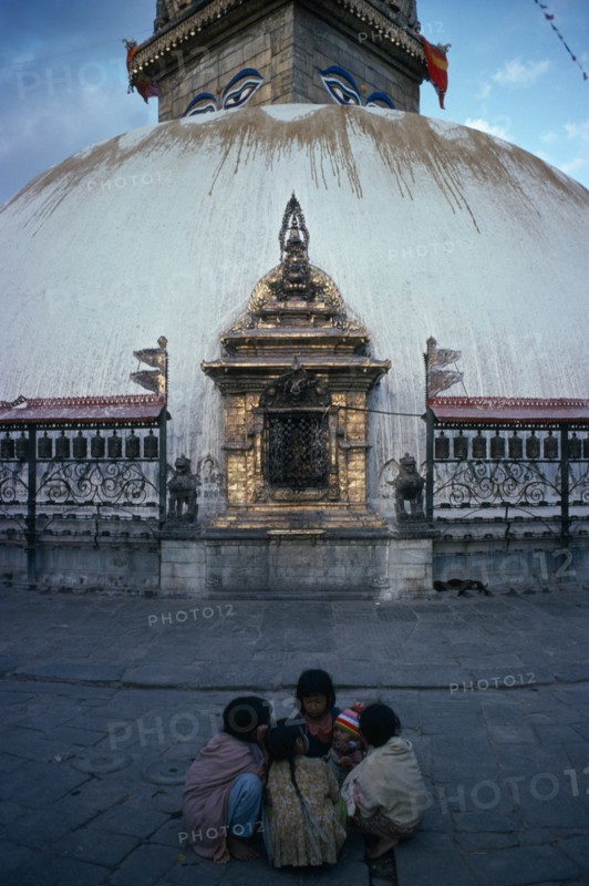 NEPAL, Kathmandu, Small group of children with baby crouched together on ground in front of Swayambhu Stupa.