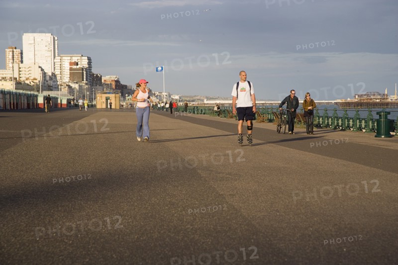 ENGLAND, East Sussex, Brighton, Woman jogging with man rollerblading on the seafront promenade.