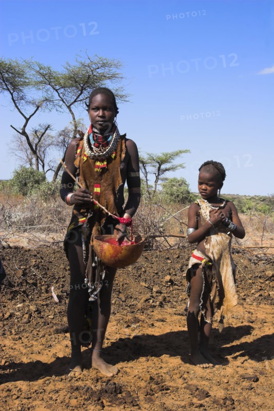 ETHIOPIA, Lower Omo Valley, Tumi, "Dombo village, Child watching Hamer lady stirring cows bood ready for drinking"