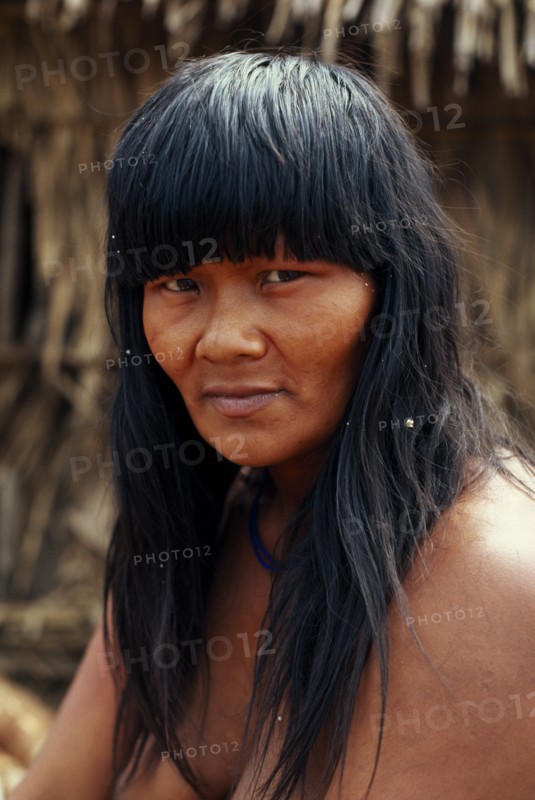 BRAZIL, Mato Grosso, Indigenous Park of the Xingu, Head and shoulders portrait of young  Panara woman outside thatched home part seen behind. Formally known as Kreen-Akrore  Krenhakarore  Krenakore  Krenakarore  Amazon American Brasil Brazilian Female Women Girl Lady Indegent Kreen Akore Latin America Latino South America Female Woman Girl Lady Immature One individual Solo Lone Solitary