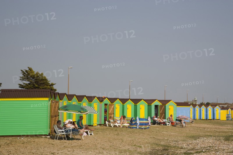 ENGLAND, West Sussex, Littlehampton, Green and yellow beach huts on shingle beach with sunbathers on sun loungers
