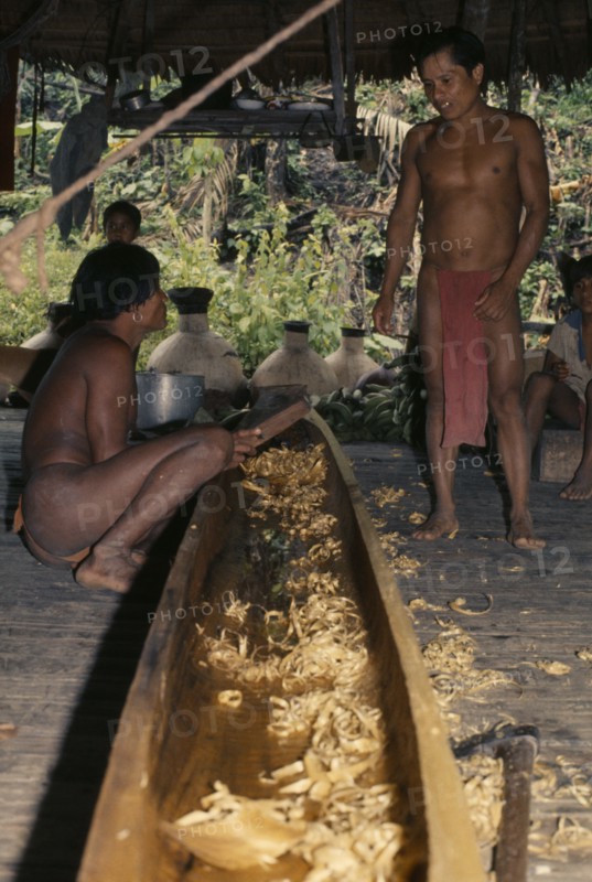COLOMBIA, Choco, Embera Indigenous People, Two Embera men discuss final shaping of wooden dug-out canoe on floor of thatched shelter beside their riverside home. Pacific coastal region boat canoa tribe American Colombian Colombia Hispanic Indegent Latin America Latino Male Men Guy South America  Pacific coastal region boat piragua tribe American Colombian Columbia Hispanic Indegent Latin America Latino Male Men Guy South America Male Man Guy 2