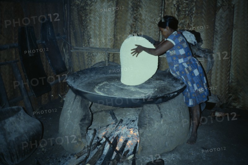 COLOMBIA, North West Amazon, Tukano Indigenous People, Barasana woman making casabe bread from manioc flour baked on large circular shallow clay oven over wood fire enclosed by clay oven wall.  Tukano sedentary Indian tribe North Western Amazonia cassava American Colombian Columbia Female Women Girl Lady Hispanic Indegent Latin America Latino South America Tukano Female Woman Girl Lady One individual Solo Lone Solitary