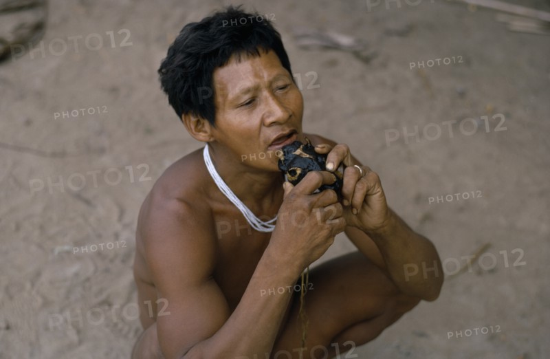 COLOMBIA, North West Amazon, Tukano Indigenous People, Barasana shaman playing deer skull flute outside the maloca/large communal home. Tukano sedentary Indian tribe North Western Amazonia American Colombian Columbia Hispanic Indegent Latin America Latino Religion South America Tukano One individual Solo Lone Solitary Religious