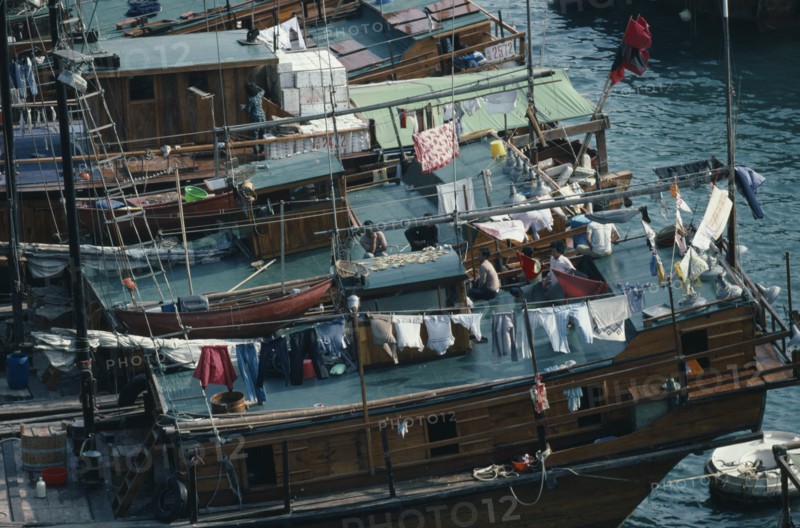 HONG KONG, Aberdeen Harbour, Sampan homes anchored in the harbour.  People and belongings on decks hung with washing.  Fish drying on roof of boat in foreground.