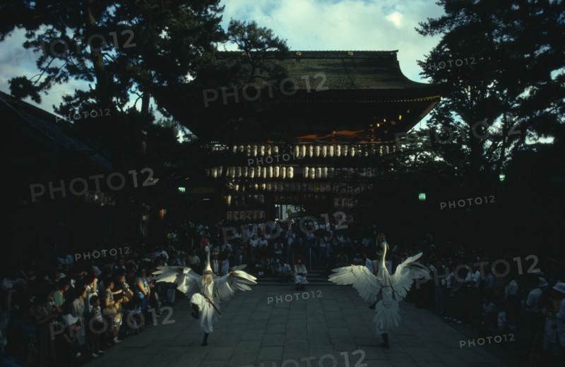 JAPAN, Honshu, Kyoto, "Gion District, Yasaka Shrine.  Performance of the Dance of the White Herons in outside courtyard watched by large crowd.  Believed to have originated in the ninth century as a feature of Shinto rituals to rid Kyoto of disease, remains part of the festival activities to this day."