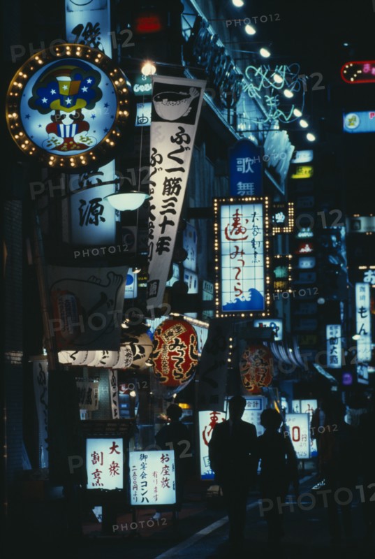 JAPAN, Honshu, Tokyo, "City street scene at night with illuminated neon signs advertising bars, restaurants and other entertainments.  Couple walking in picture centre."