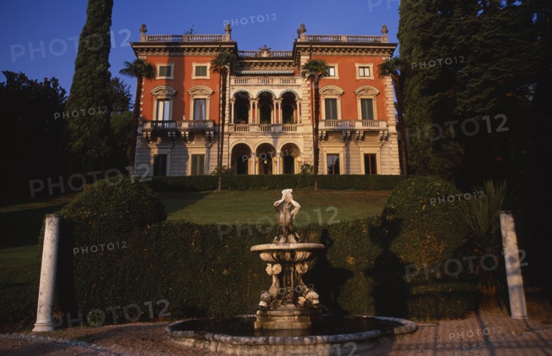 ITALY, Lombardy, Lake Como, "Private villa and formal gardens near Tremezzo, stone fountain in immediate foreground with lawn enclosed by hedge and grand facade of house behind."