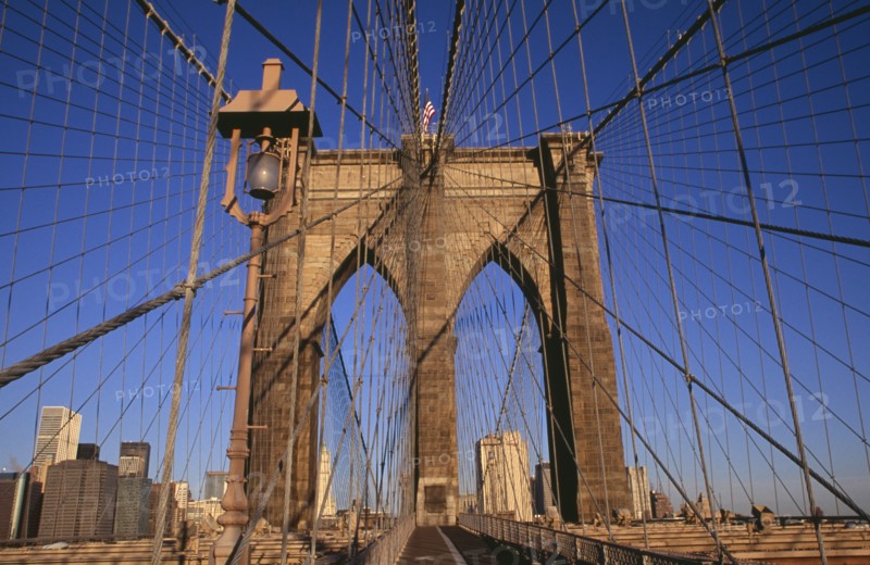 USA, New York, New York City, Brooklyn Bridge.  View across bridge towards Manhattan skyline part framed by central stone tower and intersected by steel wires and suspension cables. Spans the East River.  Construction began in 1870 and the bridge opened for use in 1883.