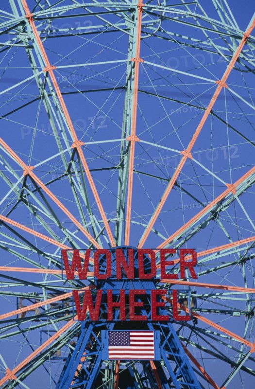 USA, New York, New York City, Coney Island.  Ferris wheel painted blue and orange with sign in red ‘Wonder Wheel’ and American Stars and Stripes flag below.  Cropped to fill frame.