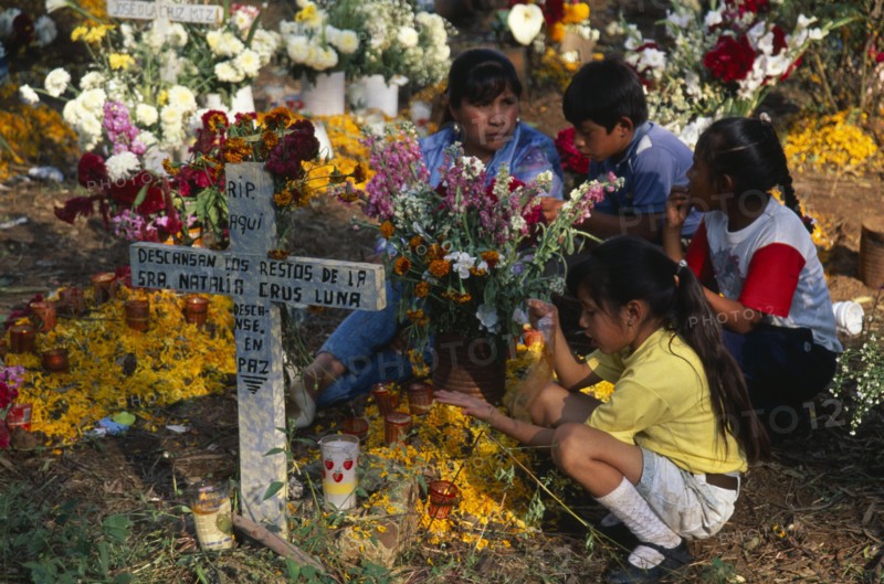 MEXICO, Michoacan, Patzcuaro, Tzurumutaro Cemetery.  Children by family grave decorated with candles and flowers for the Day of the Dead.