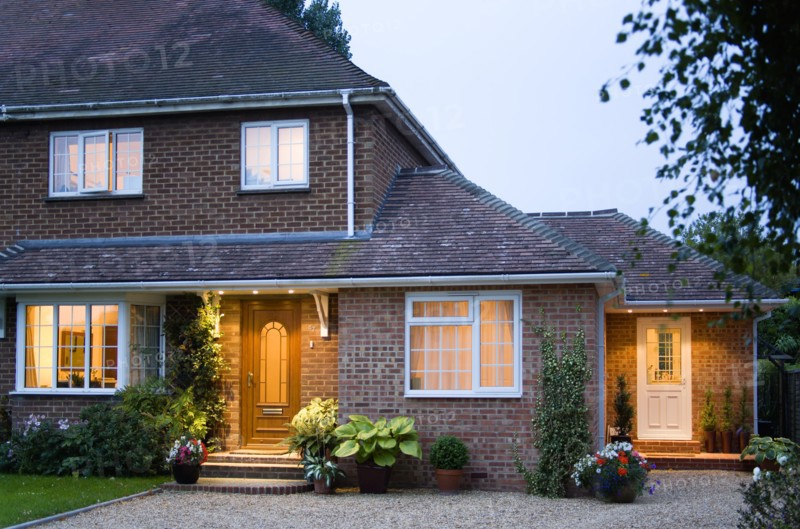 ARCHITECTURE, Buildings, Homes, Semi detached house brick built and garden with gravel driveway at dusk with lights on in windows and above external doors