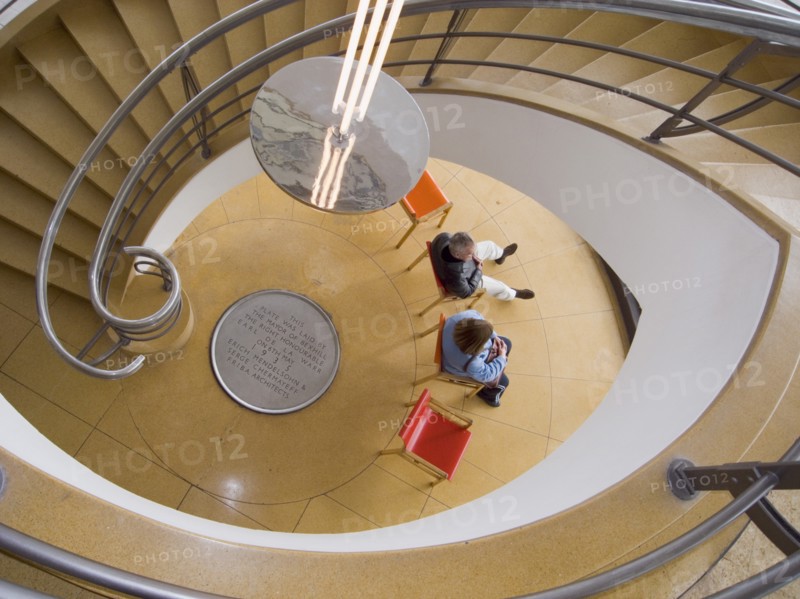 ENGLAND, East Sussex, Bexhill-on-Sea, The De La Warr Pavilion. Interior view down the helix staircase with chrome Bauhaus globe lamps. People sitting on colourful chairs at the bottom