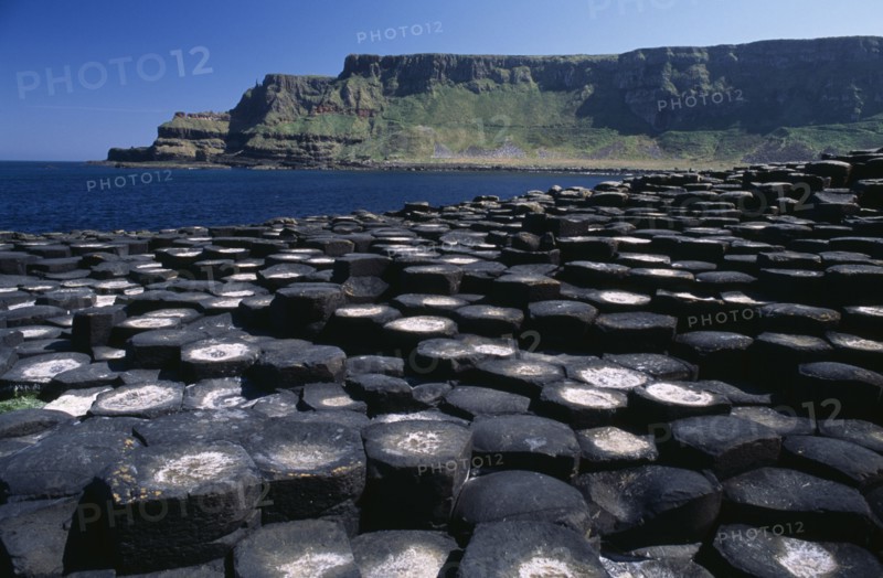 NORTHERN IRELAND, Co Antrim, Giants Causeway, Interlocking basalt stone columns left by volcanic eruptions. View across the stones towards the east from the main section with cliffs and coastline