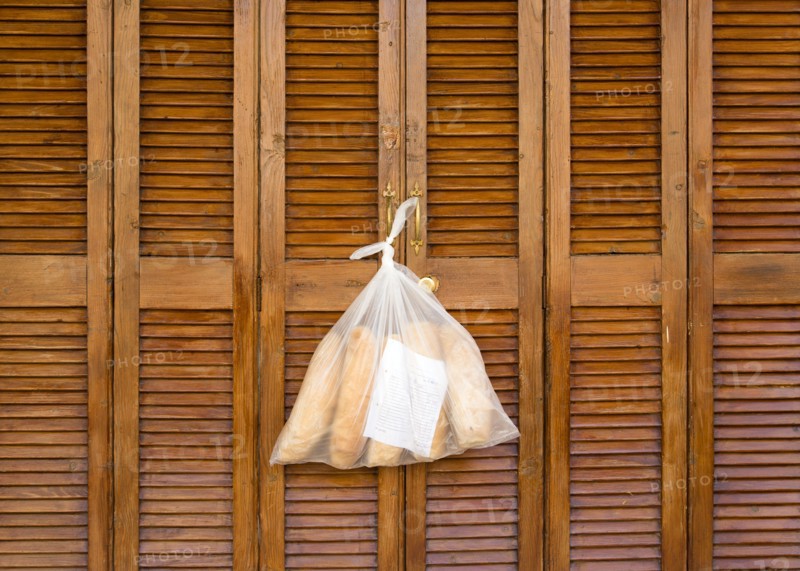 MALTA, Saint Julians, Plastic bag containing loaves of fresh bread tied to the handle of wooden louvre shutter doors