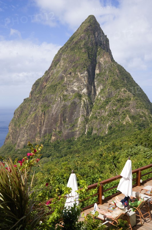 WEST INDIES, St Lucia, Soufriere , Val des Pitons The volcanic plug of Petit Piton and the lush valley seen from the sun deck of the Ladera Spa Resort Hotel with tourists sunbathing on sunbeds beside umbrellas