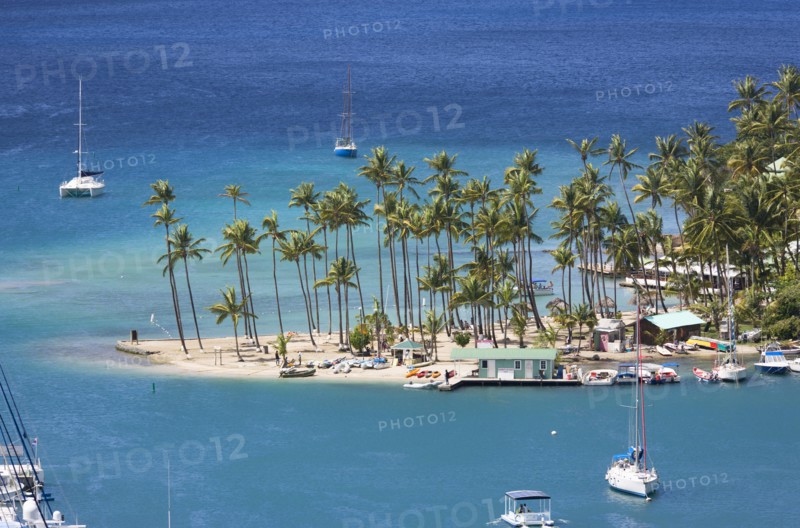 WEST INDIES, St Lucia, Castries , Marigot Bay Yachts at anchor beyond the small coconut palm tree lined beach of the Marigot Beach Club sitting at the entrance